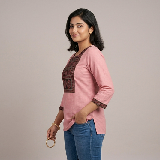 Woman wearing a pink short top with patterned sleeves and blue jeans on a plain background